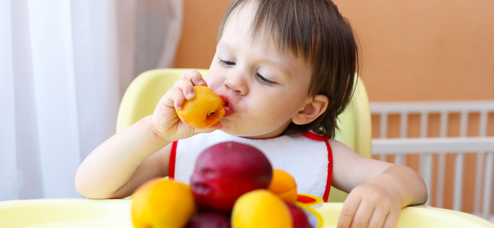 Bebê branco comendo manga em cima da mesa