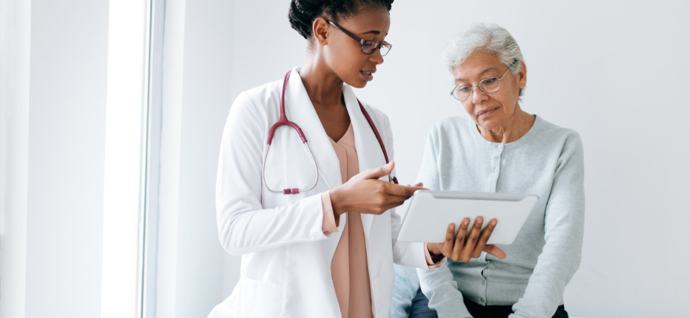 Médica de pele negra de cabelos presos consultando a paciente de pele negra de cabelos curtos e brancos